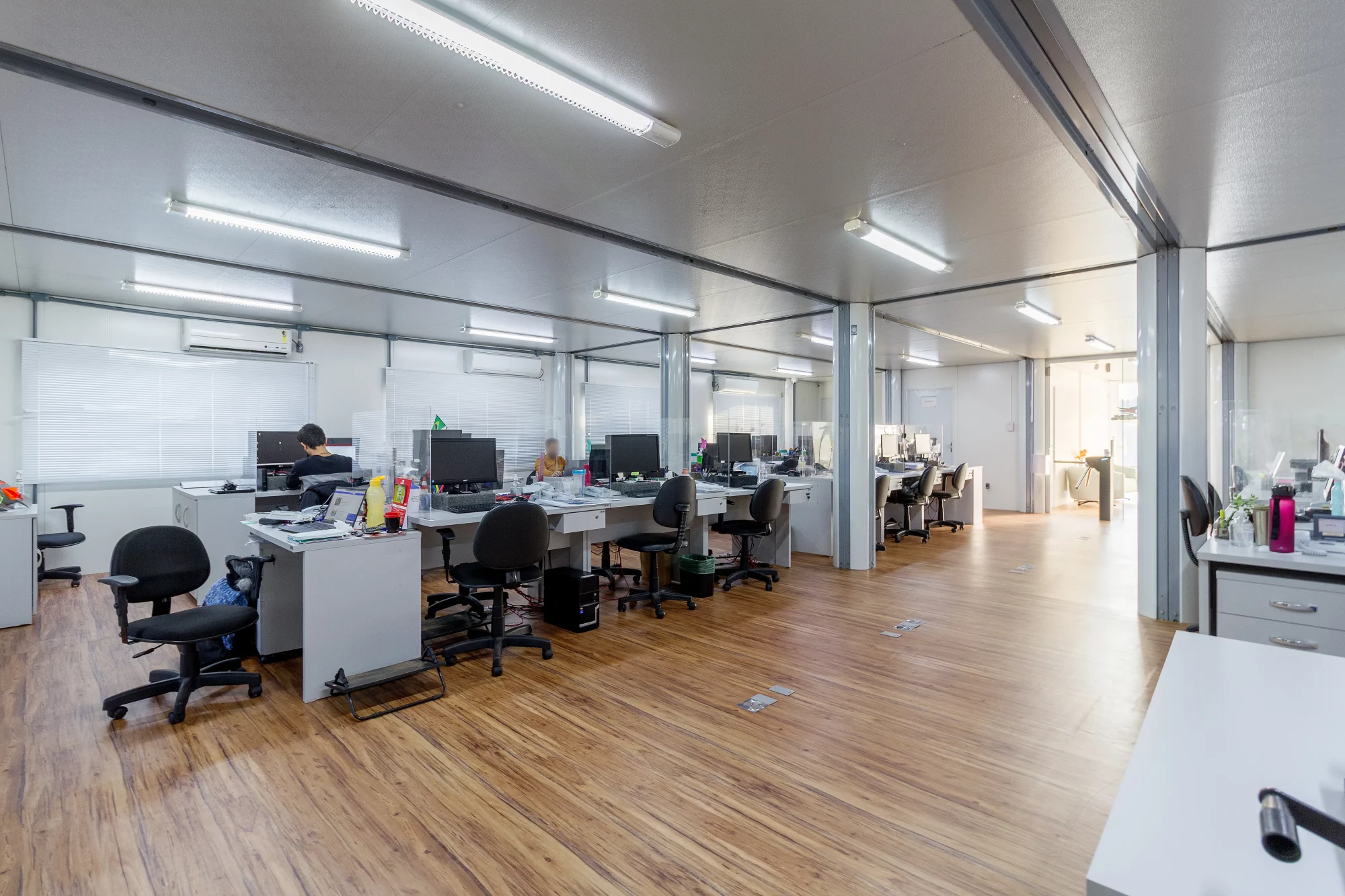 Escritório container com bancada de trabalho e janelas amplas.